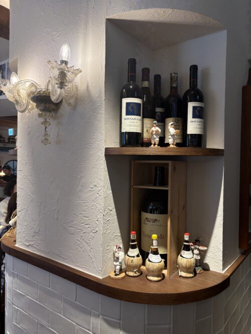 難波「サンタアンジェロ」店内のワインボトルが並ぶ飾り棚。イタリア製の土器ボトルとシェフのミニチュア人形。