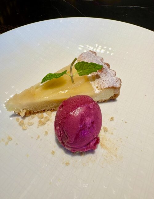 白い皿に美しく盛り付けられた、タルトケーキと、ベリー系の鮮やかなシャーベット。ミントの葉と粉砂糖で飾られている。
