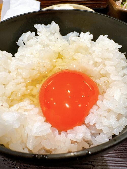 炊き立ての白米の中央に、濃厚なオレンジ色の生卵の黄身が完璧な形で乗せられた卵かけご飯(TKG)のクローズアップ。